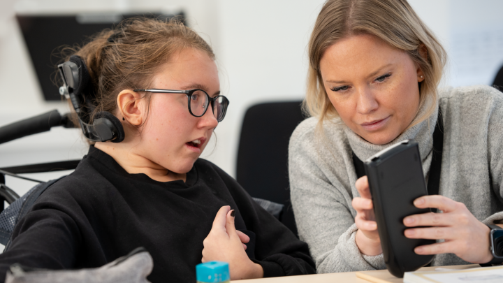 Bilden visar en elev och en vuxen person som tittar på en mobiltelefon tillsammans.