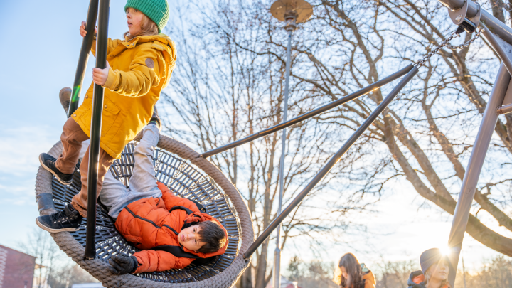 Två barn gungar i en stor nätgunga, ena barnet står upp och andra barnet ligger ner i gungan.