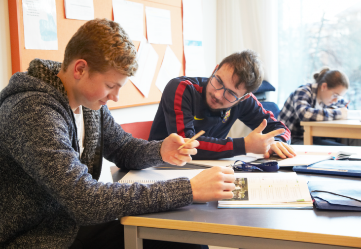 Tre elever i ett klassrum. Två av dem samtalar och löser en uppgift tillsammans.