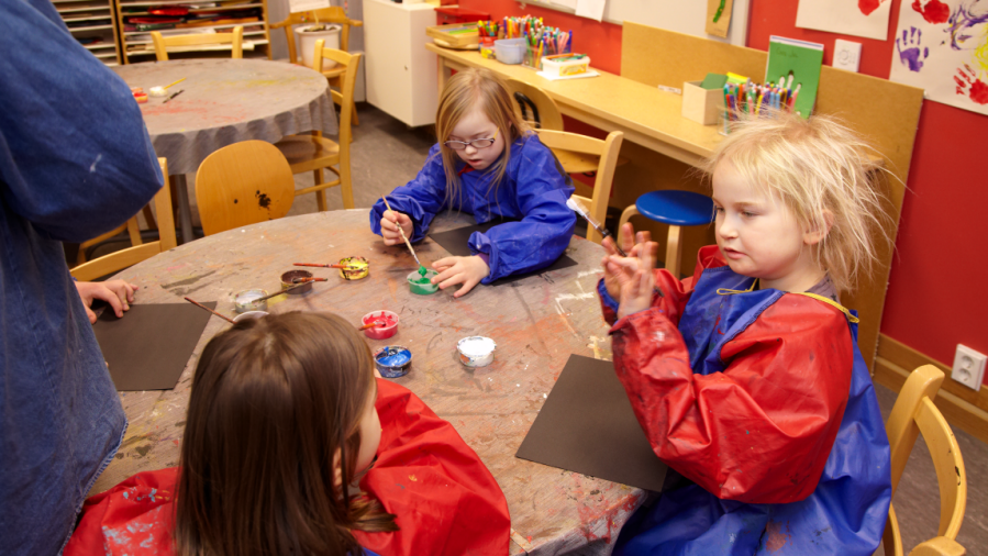 Tre barn sitter runt ett bord och målar med vattenfärg.