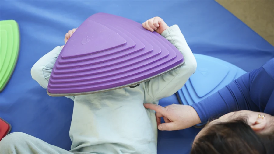 Barnet ligger på mattan och täcker sitt ansikte med en lila platta av skumgummi.