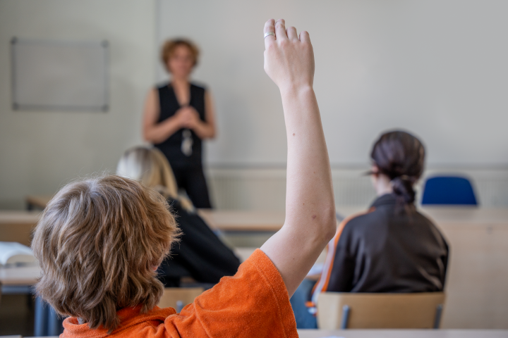Bilden visar en elev som räcker upp handen i ett klassrum.