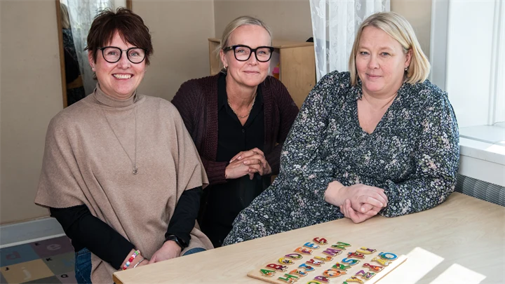 Tre personer som sitter vid ett bord. På bordet finns en siffertavla.