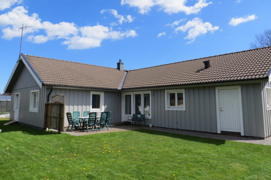 Baksidan av ett grått hus, en gräsmatta och trädgårdsmöbler.