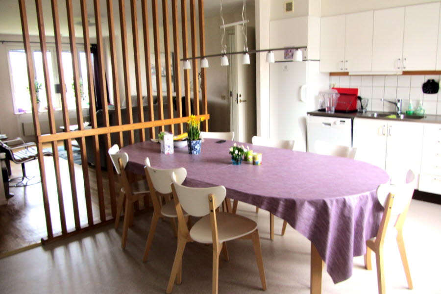Ett kök med matbord och träspalje som avskiljare till vardagsrummet.