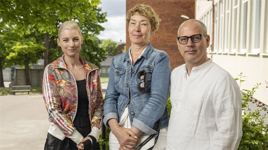 På bilden står Ylva Bergh, Misan Berge och Lars Martinsson bredvid varandra vänd mot kameran. Bakom dom syns en skolbyggnad.