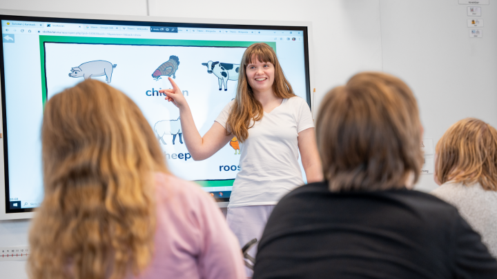 Bilden visar en lärare som pratar med klassen och pekar på bildstöd på en skärm.