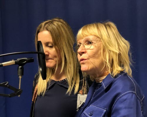 Porträtt på två personer som står i en studio och pratar i en mikrofon