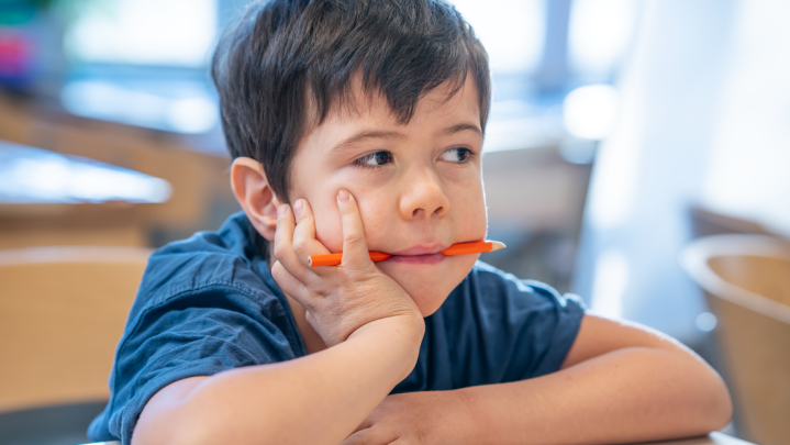 Elev sitter vid skolbänken med en penna i munnen