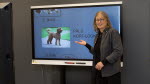 Läraren Ulrika står framför en skärm och pekar på en hund med lockig päls. 