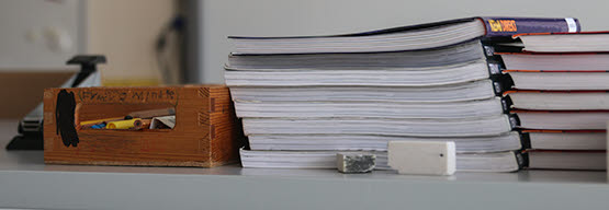 Närbild från sidan på böcker som ligger i flera högar på ett bord.