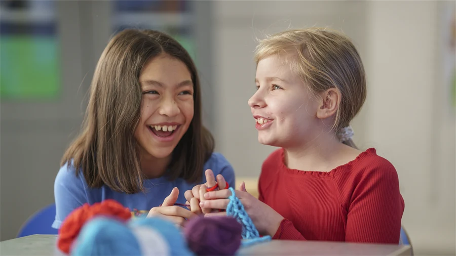 Två barn skrattar vid ett bord samtidigt som de stickar.