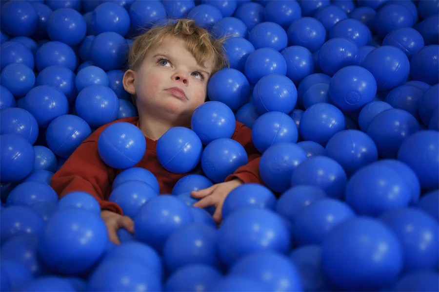Ett barn ligger i ett bollhav med blå bollar och tittar upp mot taket.