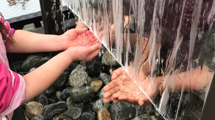 Barnhänder som känner på rinnande vatten.