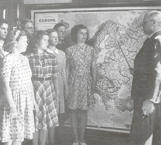 Några flickor står vid Nordenkartan och en manlig lärare framför dem