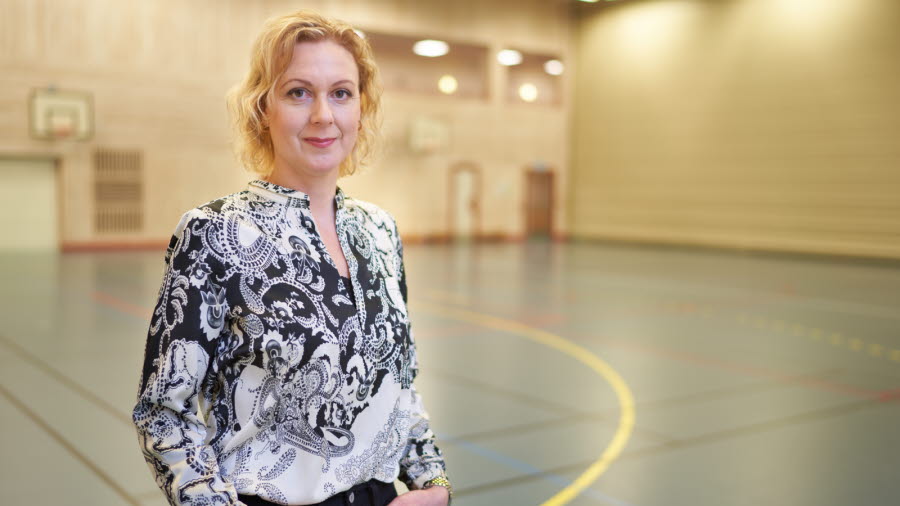Bilden visar Karin Fröding, en blond kvinna som står och tittar in i kameran. Karin bär en svartvit mönstrad blus och ett par svarta byxor.