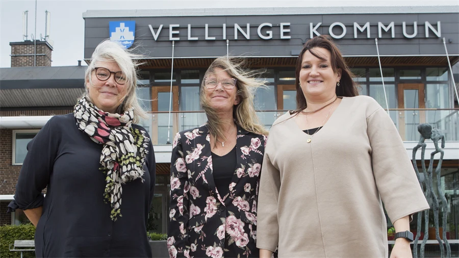Tre vuxna personer står framför en skylt med texten Vellinge Kommun.