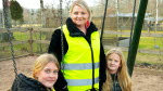 En lärare i gul reflexväst står med två elever vid en gungställning på en skolgård
