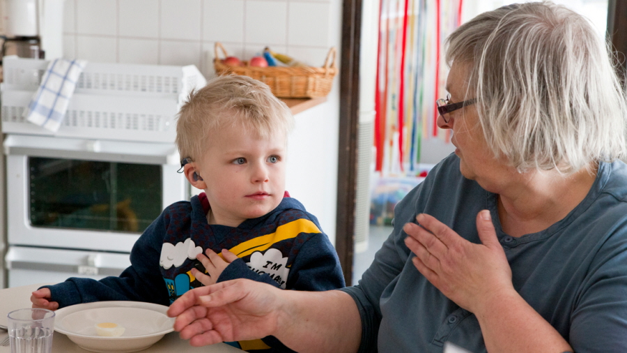 Bilden visar en pojke med hörapparat i förskolan som lyssnar på en pedagog
