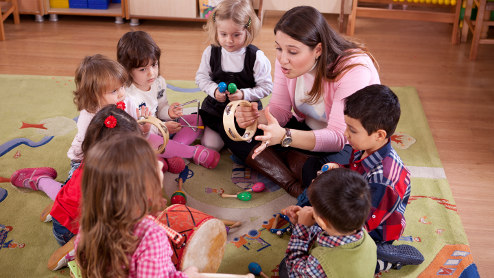 Barnen sitter samlade i en cirkel på golvet och leker med instrument tillsammans med läraren.