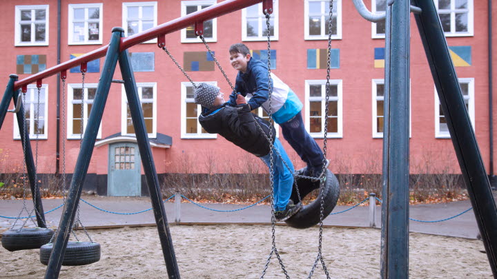Två barn gungar tillsammans på en skolgård.