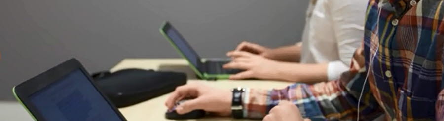Bilden visar två personer som sitter vid ett bord med varsin bärbar dator framför sig.