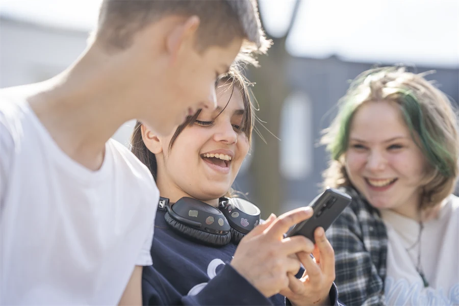 Tre elever i tonåren tittar på något på en telefon tillsammans.