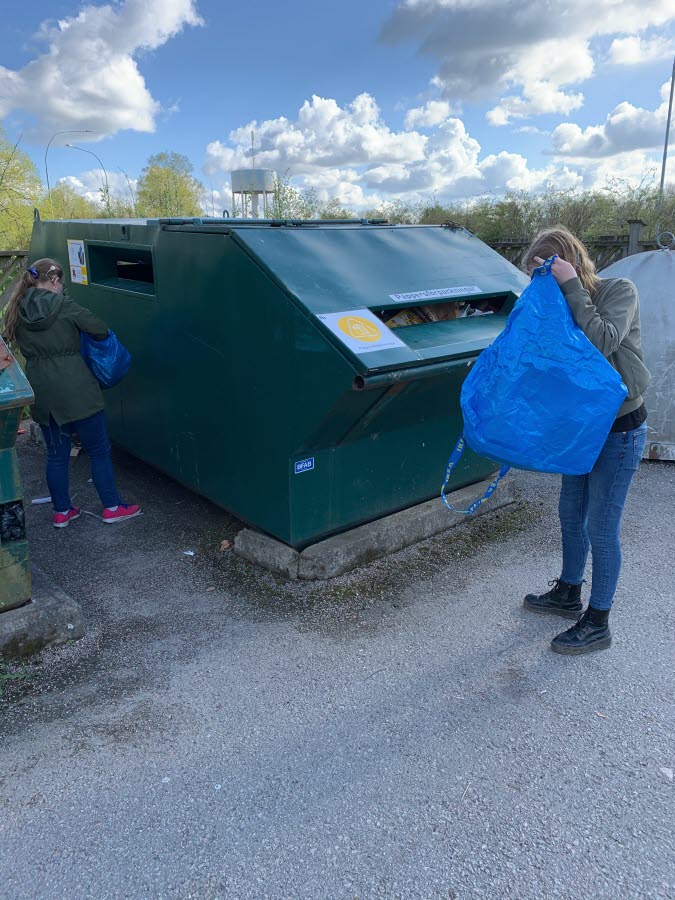 Två elever sorterar från sina kassar och kastar i återvinningsplatsen.