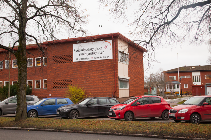 Åsbackaskolans skolbyggnad. I förgrunden syns flera parkerade bilar.