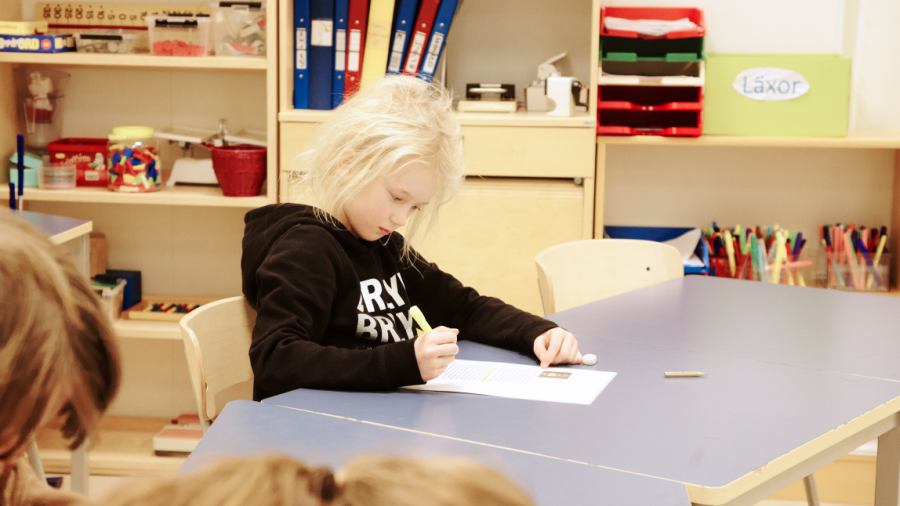 En liten flicka sitter vid ett bord och skriver på ett papper.