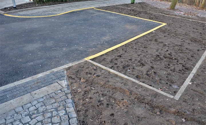 Bilden visar en målad gul linje som förtydligar gränsen mellan asfalten och jorden som ska planteras.