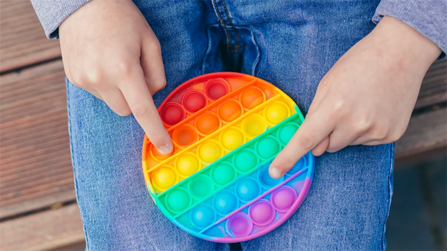 Händer med regnbågsfärgad pop it fidget toy