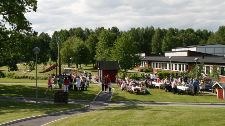 Bilden visar Ekeskolans skolbyggnad och skolgård. Vi ser många elever och lärare som har samlats på skolgården.