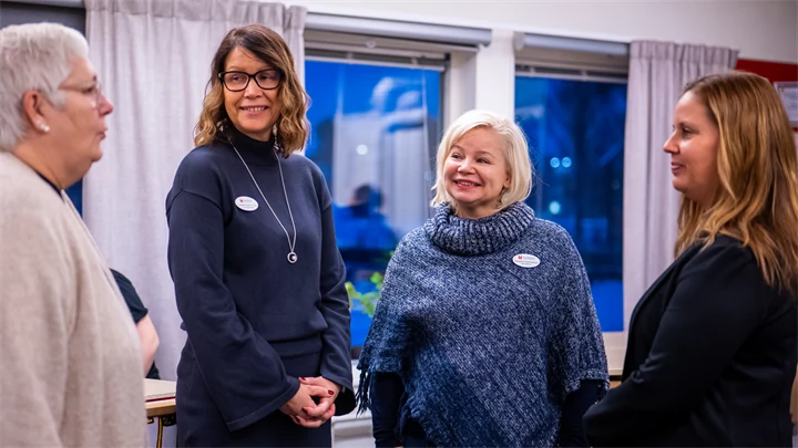 Fyra kvinnor står i en halvcirkel. En av dem pratar och de andra tittar på henne.